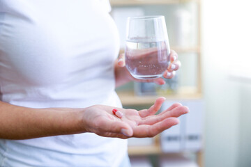 Closeup shot of an unrecognisable woman holding a glass of water and medication in the room.
