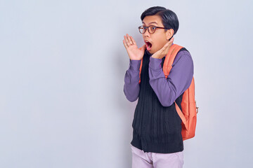 Surprised young Asian student man in casual clothes with backpack  looking away with open mouth isolated on gray background. High school university college concept