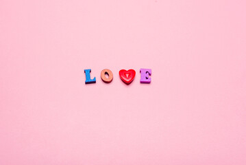 Word LOVE made of wooden letters and a heart on a pink background