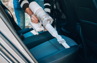 Close-up of a man vacuuming a car seat. The hand holds a cordless vacuum cleaner and cleans the...