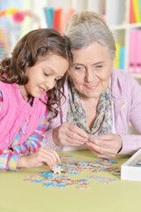 Fototapeta premium Grandmother with granddaughter collecting puzzle at home