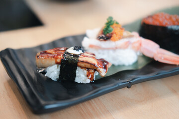 Selective focus on foie gras sushi with a blur of other sushi on the rectangular black ceramic plate.