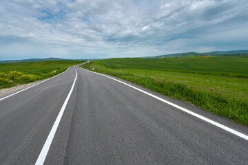 Asphalt road amidst the green hills of Tuscany, Italy