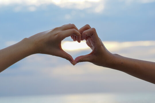 Sunlight shines through hands interlaced in heart shape on evening sky background. soft and selective focus.