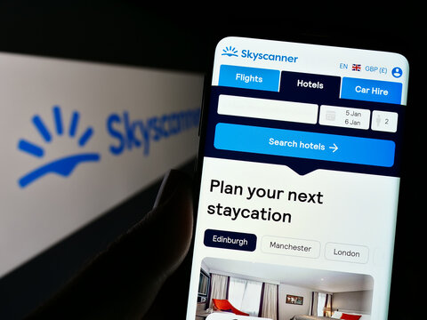 Stuttgart, Germany - 12-30-2022: Person holding smartphone with webpage of travel metasearch company Skyscanner Ltd. on screen in front of logo. Focus on center of phone display.