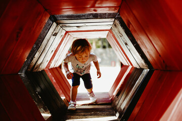 Kid playing in adventure park. Red wooden tunnel passing through. 