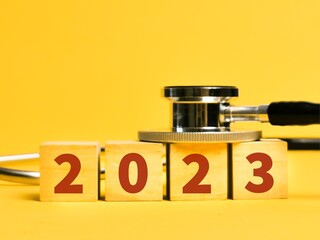 Stethoscope with 2023 number on wooden cubes against yellow background.