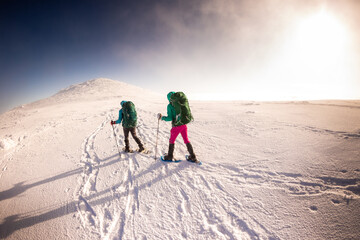 two girls with a backpack and snowshoes walk in the snow during a snow storm.