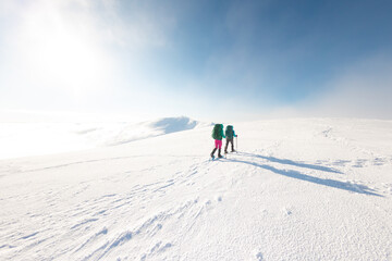 two girls with a backpack and snowshoes walk in the snow during a snow storm.