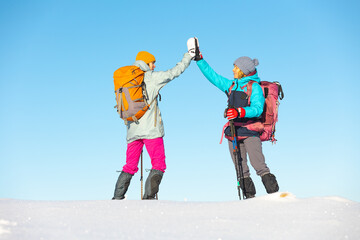 Two women walk in snowshoes in the snow, high five