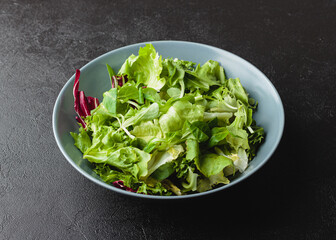 Green salad leaves in bowl on black table.
