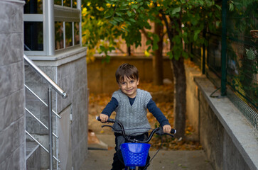 A preschool boy is smiling while riding a bicycle in a garden in autumn.