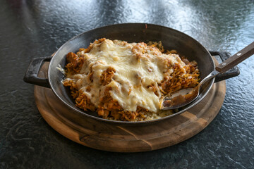 Fried rice with spices and topped with cheese in an iron pan on a wooden cutting board and a black table, fusion food, selected focus, narrow depth of field
