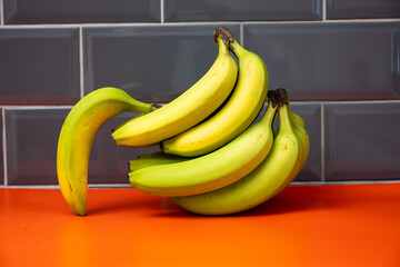 loose unripe bananas  on an orange base against a grey background