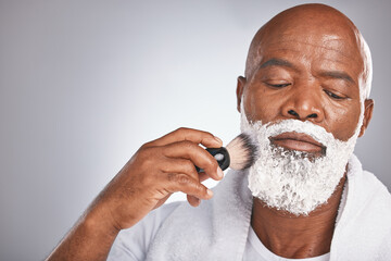 Face, shaving cream and black man with brush on beard, skincare spa treatment on grey background. Health, mock up and facial hair, mature man morning shave routine with space for product placement.