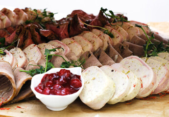 Meat platter on a wooden tray. Cold appetizer of chicken roll, beef tongue, beef with sauce