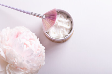 colored brush for applying a cream mask on a light background with a delicate peony flower