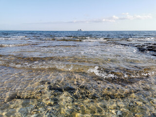 The Mediterranean Sea, in which a white pleasure yacht floats against a blue sky with clouds.