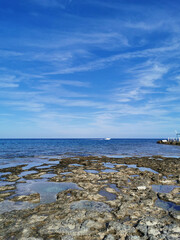 Long-hardened lava, the shore of the Mediterranean Sea against the backdrop of the sea with a white yacht and a blue sky with beautiful clouds.