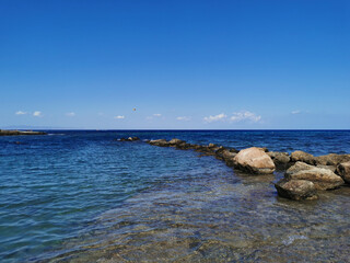 The coast of the Mediterranean Sea, waves, clear water, a stone ridge against a blue sky with clouds.
