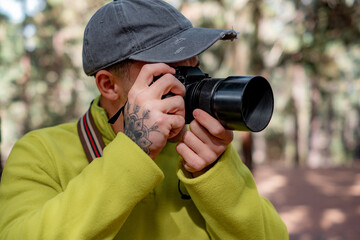 Young photographer with hat working taking capture photo of nature in the woods holding and using his camera in autumn or winter time