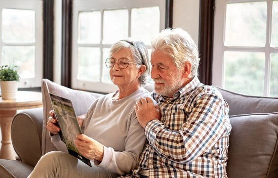 Smiling senior couple sitting together on the couch watching a brochure of the Garajonay de La Gomera national park. Happy elderly couple relaxing while planning a trip