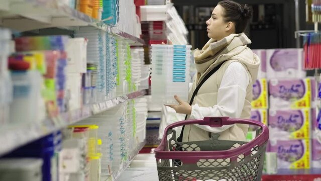 A young female customer chooses household goods while shopping in the kitchen section of a large hypermarket with a large assortment in a home goods store.