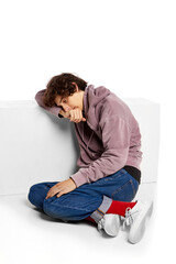 Portrait of young boy sitting on floor in despair and sadness over white background. Suffering from...