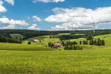 Hilly landscape in Black Forest with meadows and lonely farmhouses, wind turbines on green hills...