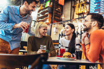Smiling young friends drinking craft beer in pub