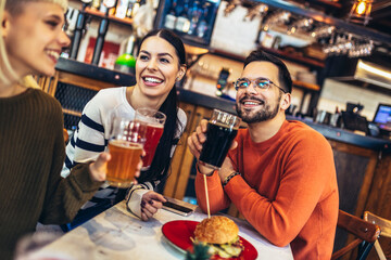 Smiling young friends drinking craft beer in pub