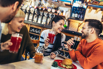 Smiling young friends drinking craft beer in pub