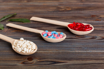 Vitamin capsules in a spoon on a colored background. Pills served as a healthy meal. Red soft gel vitamin supplement capsules on spoon