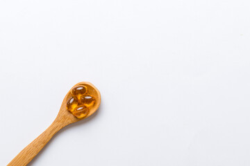 Vitamin omega capsules in a spoon on a colored background. Pills served as a healthy meal. Red soft gel vitamin supplement capsules on spoon
