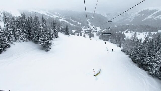 POV Empty chairlift over ski slope with big pine trees at ski resort during winter