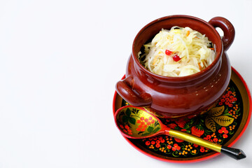 Sauerkraut in a clay pot on wooden Khokhloma plate and spoon isolated on white