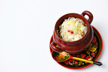 Sauerkraut in a clay pot on wooden Khokhloma plate and spoon isolated on white.