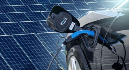 Close up of electric car with a connected charging cable on the background of solar panels	