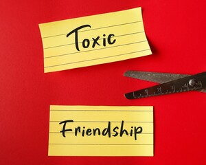 Scissors cutting note paper with handwritten TOXIC FRIENDSHIP, refers to friends who leave negative...