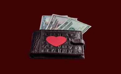 Brown leather wallet with red heart. Dollars stick out of the wallet. Close-up. The concept of cash costs for the purchase of gifts for Valentine's Day, wedding, birthday.