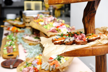 Buffet table with cold appetizers. Meat and vegetable snacks are placed on wooden stands. Stand with brusettas in the foreground