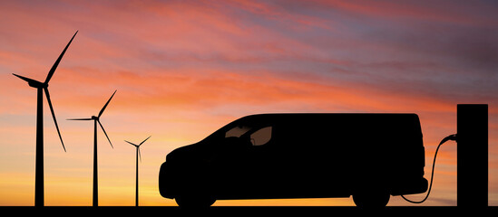 Silhouette of electric van with charging station and wind turbines on a background of sunset sky