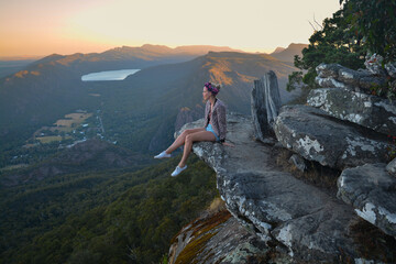 Woman sitting on rock dangling feet off mountain top
