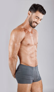 Fitness, body and man in underwear in a studio for health, wellness and exercise for muscle. Happy, smile and muscular male model from Puerto Rico isolated by a gray background after a workout.