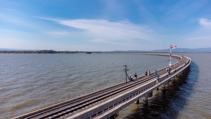 Obraz premium Aerial view of an amazing travel train parked on a floating railway bridge over the water of the lake in Pa Sak Jolasid dam with blue sky at Lopburi, Thailand.