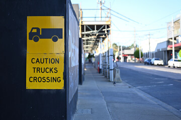 A yellow caution trucks crossing sign, with icon of a truck, on black hoarding outside a construction site