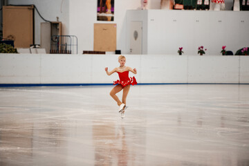 a little girl in a red dress participates in a figure skating competition	