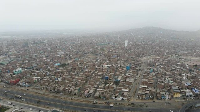 Drone shot of massive and crowded neighborhood next to a highway in Ventanilla in the district of San Juan de Miraflores. Lima, Peru