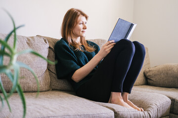 Caucasian woman in casual clothes reading her diary relaxing in the living room.