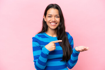Young Colombian woman isolated on pink background holding copyspace imaginary on the palm to insert an ad